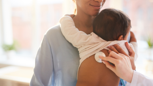 Mother holding child while a doctor holds a stethoscope on their back